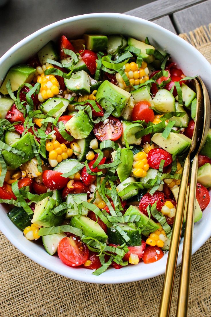 a salad with cucumbers, tomatoes, corn and lettuce in a white bowl