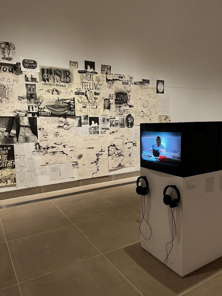 a television sitting on top of a white pedestal in front of a wall covered with pictures