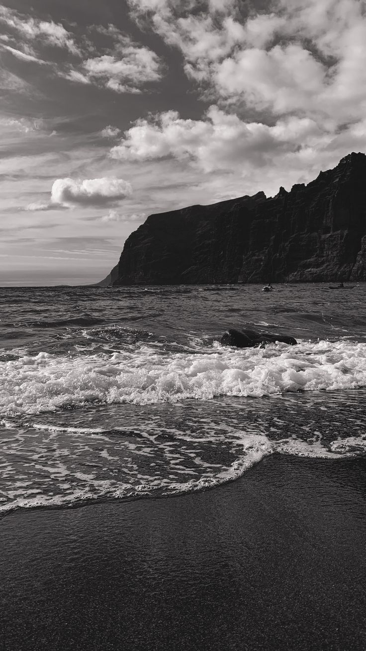 a black and white photo of the ocean with waves crashing in front of an island