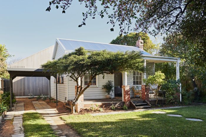 a small house with a white roof and trees in the front yard on a sunny day