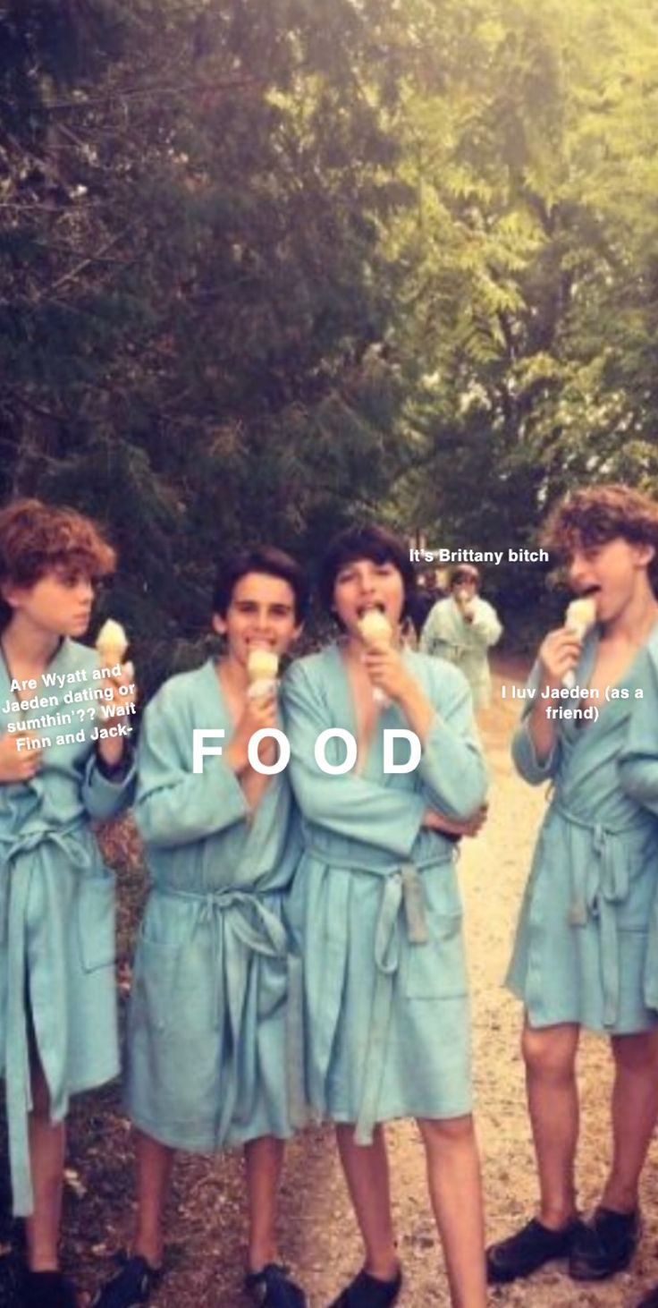 four women in blue robes are eating ice cream and posing for the camera with trees behind them