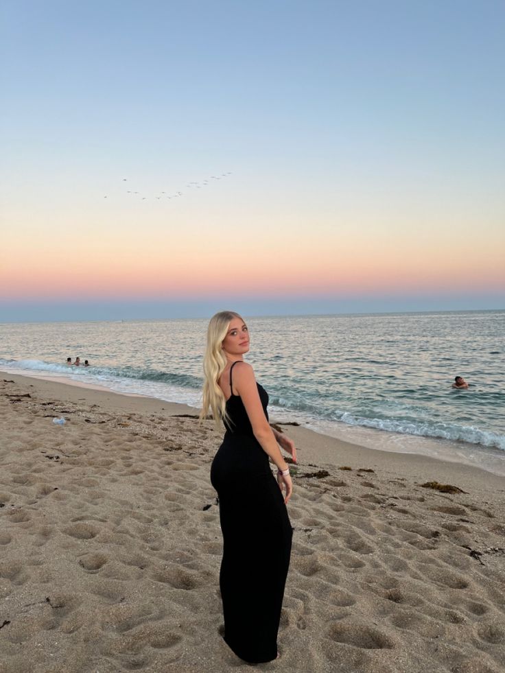 a woman standing on top of a sandy beach next to the ocean in front of a sunset