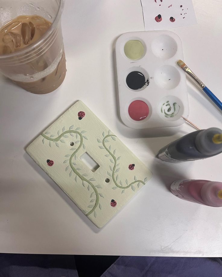 the table is covered with paints and other art supplies, including a light switch plate