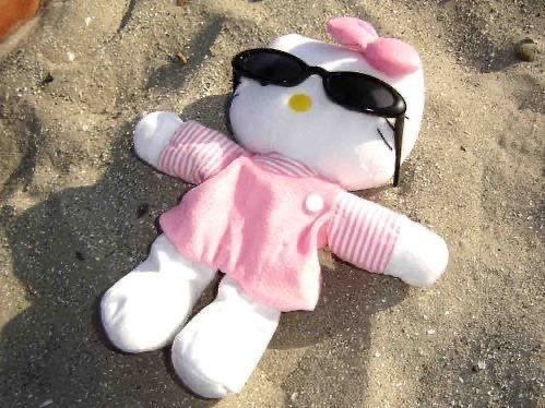 a hello kitty stuffed animal laying in the sand with sunglasses on it's head