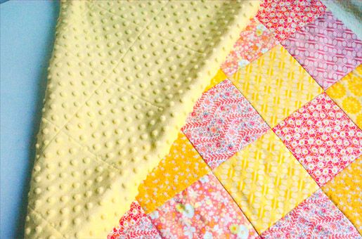 a yellow and pink quilt sitting on top of a blue table next to a piece of cloth