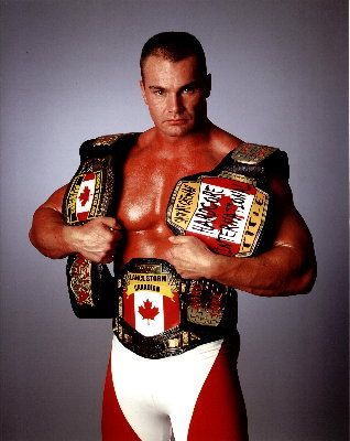 a man in red and white wrestling trunks holding his hands on his hips while posing for the camera