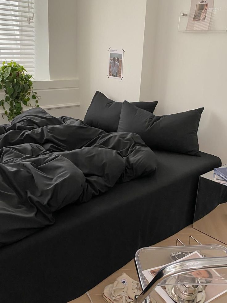 an unmade bed with black sheets and pillows on it in front of a window