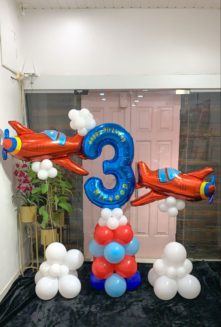 an air plane balloon arch with the number three on it and balloons around it in front of a door