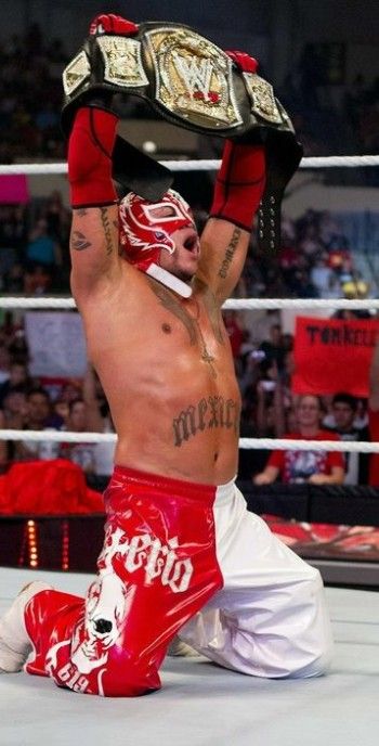 a man sitting on the ground with his arms up in the air while holding a wrestling belt