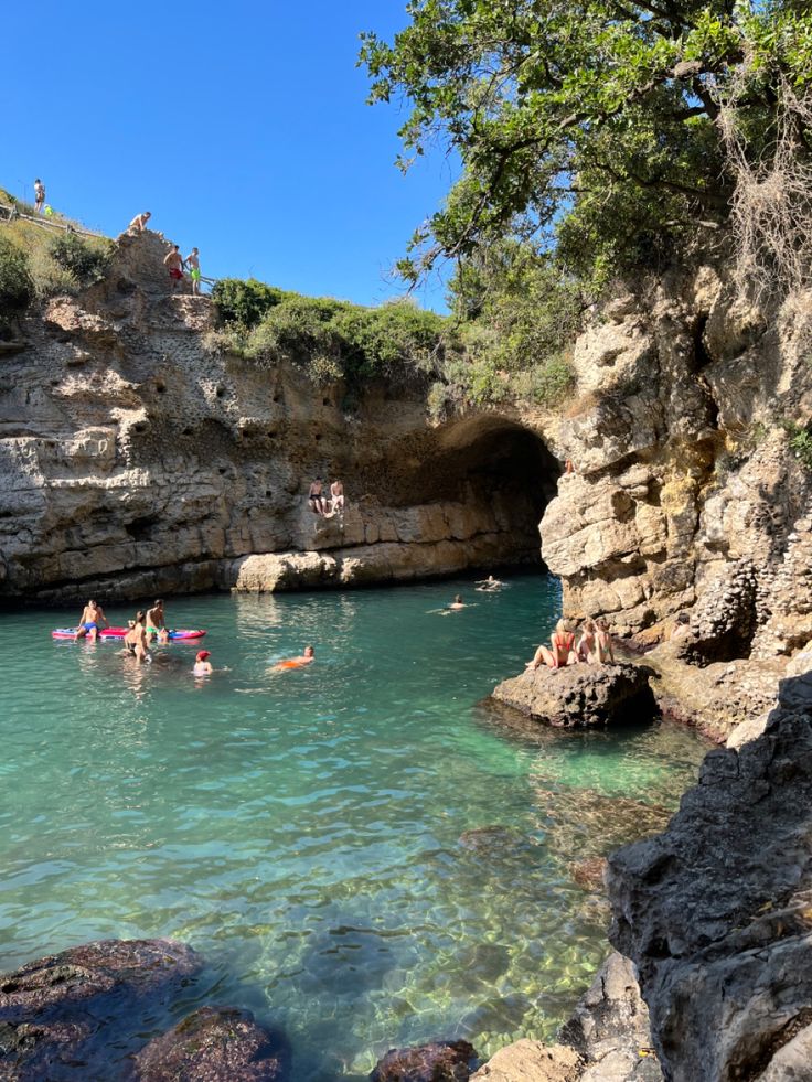 people are swimming in the water near some rocks