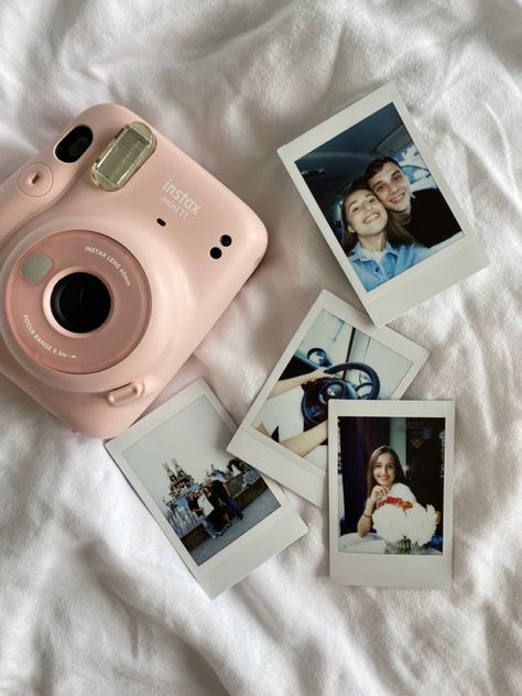 a pink polaroid camera sitting on top of a bed next to pictures and an instax