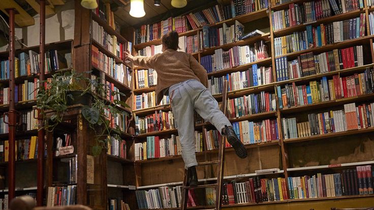 a man climbing up the side of a ladder in front of a bookshelf