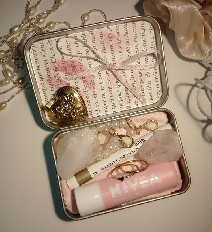 an open tin box with some items in it on top of a table next to pearls and other accessories