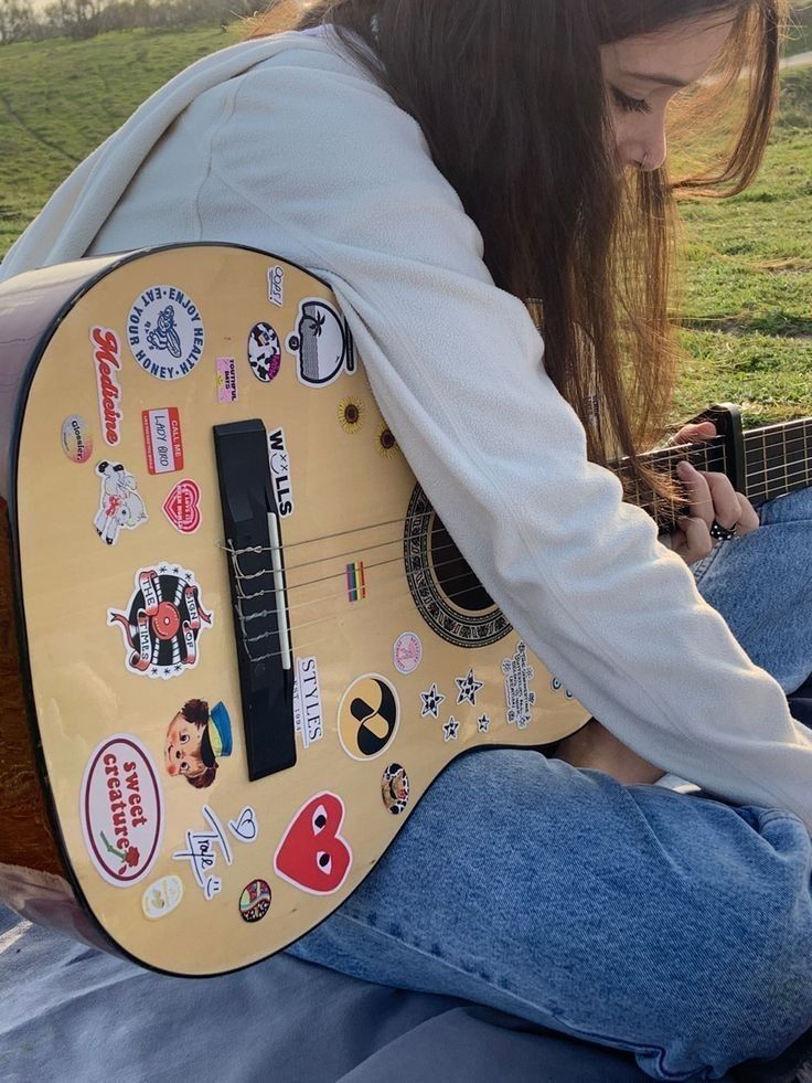 a woman sitting on the ground with a guitar in her lap and looking at it