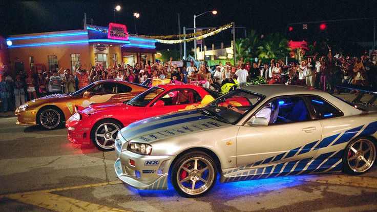 three cars parked in front of a crowd at night