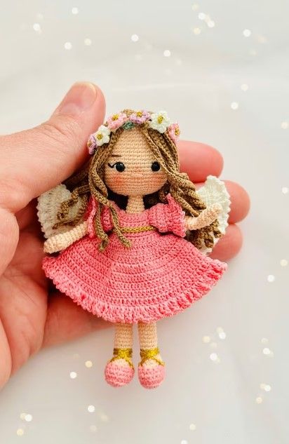 a hand holding a tiny crocheted doll in it's right hand and wearing a pink dress