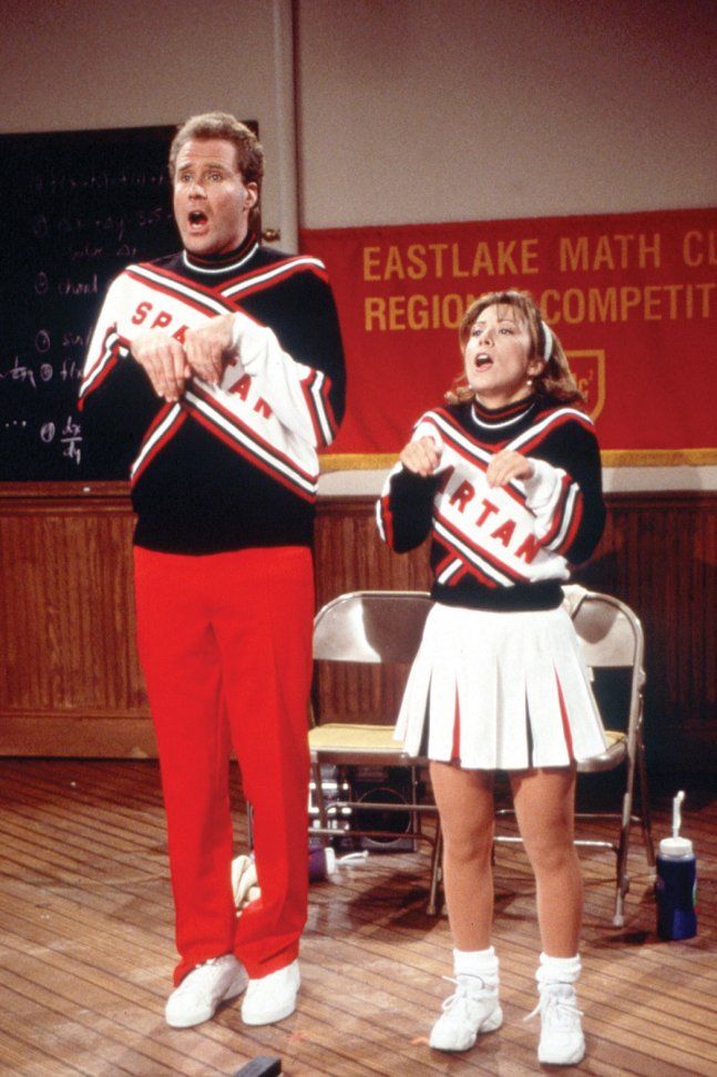 two people in cheerleader outfits standing on a stage with one holding a sign and the other singing into a microphone