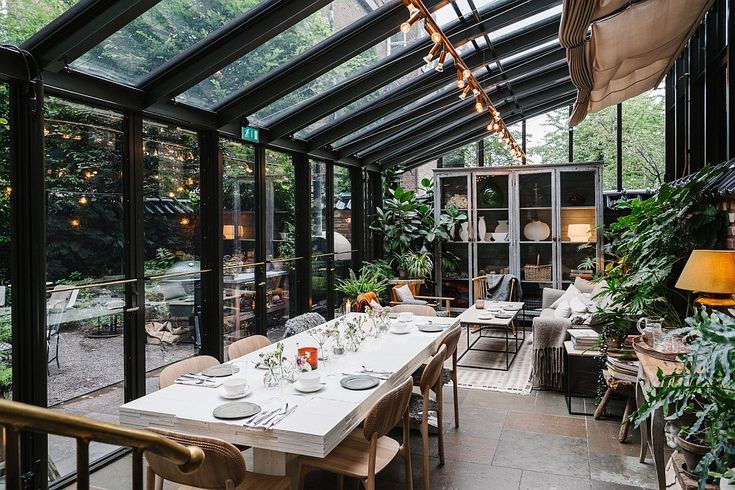 an indoor dining area with glass walls and lots of greenery on the tables in front of it