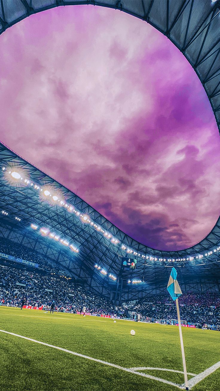 a soccer stadium filled with lots of green grass and purple clouds above it is a ball on the field