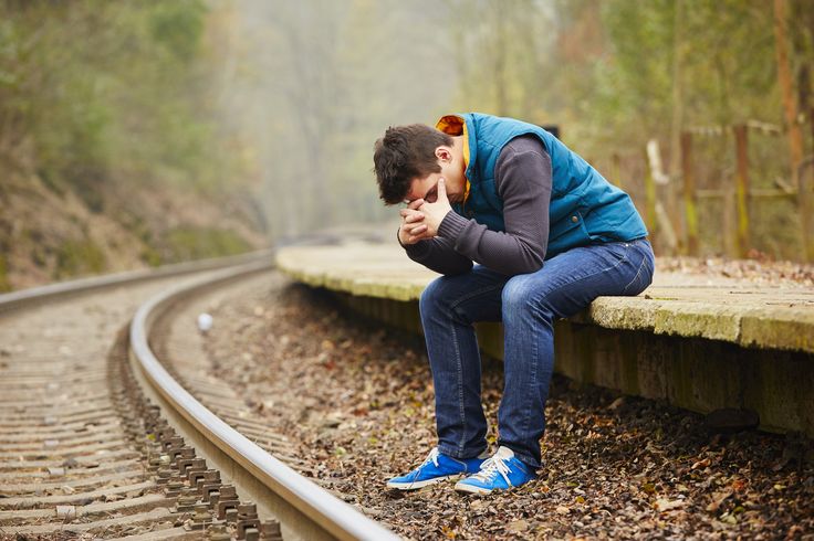 a man is sitting on the train tracks with his head in his hands and looking down