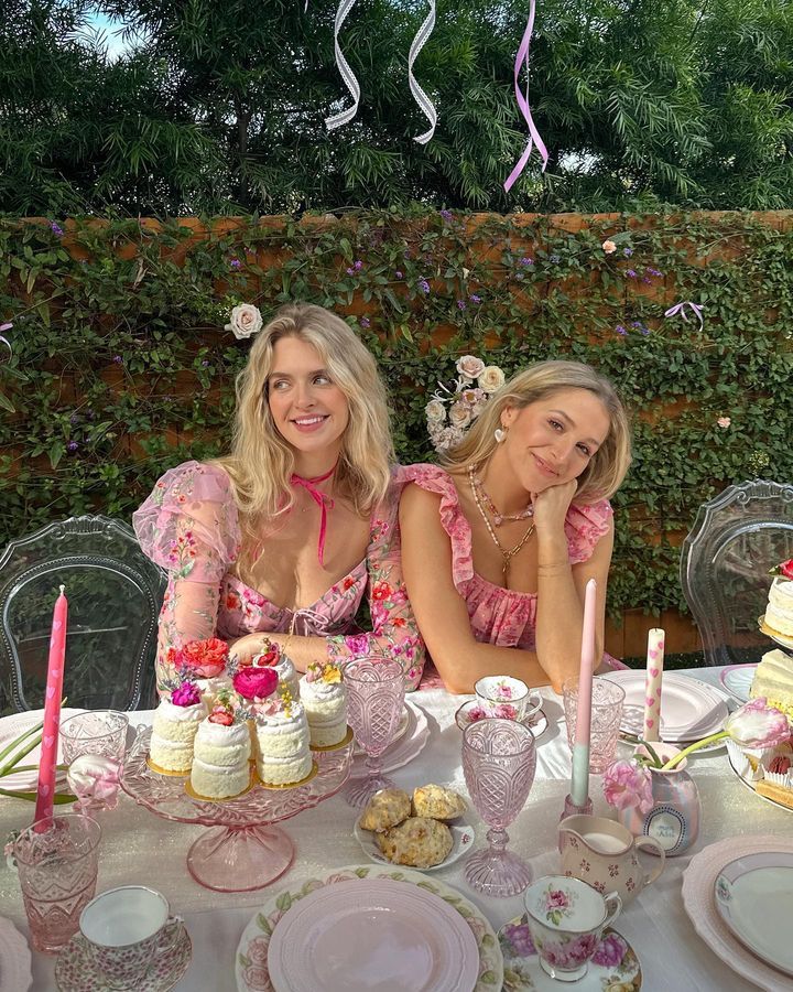 two women sitting at a table with cakes and cupcakes on it, surrounded by pink decorations