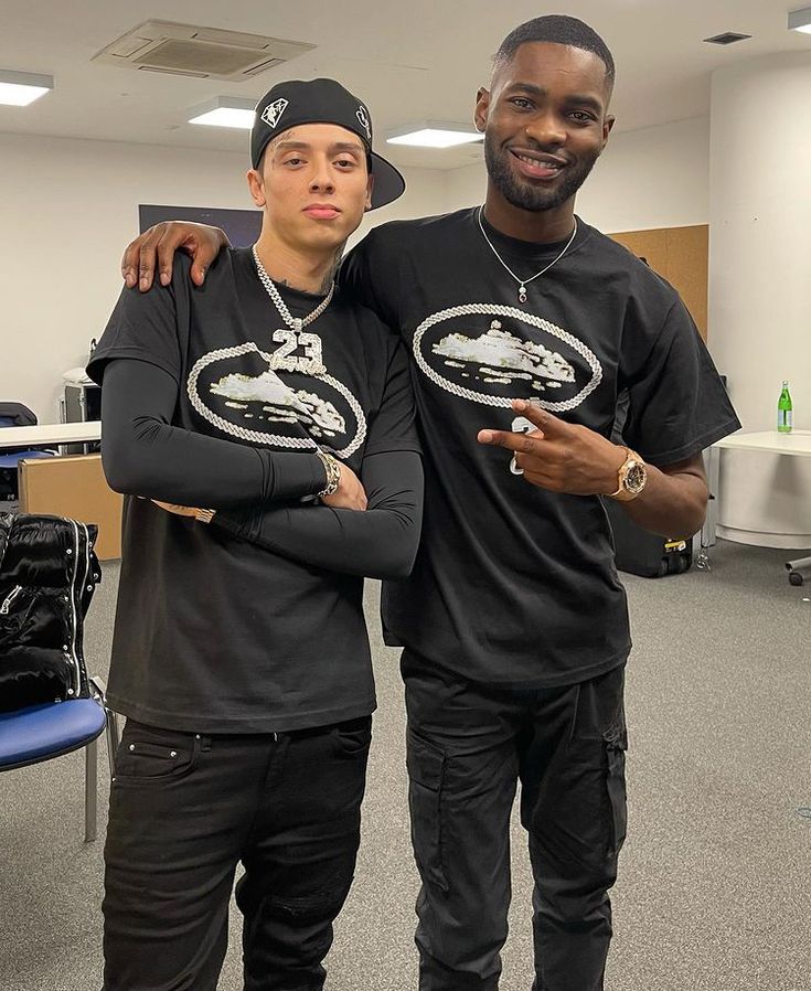 two young men standing next to each other in an office building, one with his arm around the other's shoulder