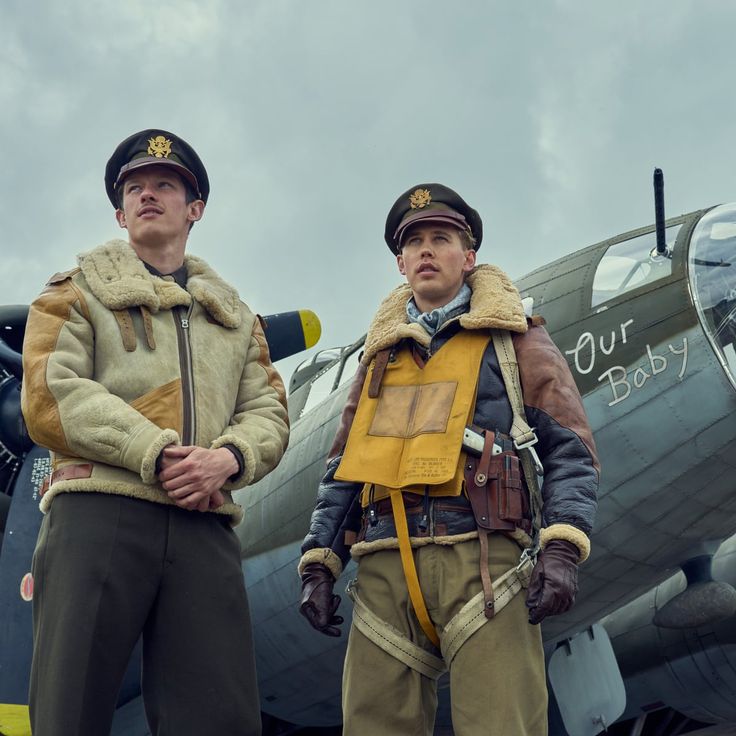 two men standing next to each other in front of an airplane