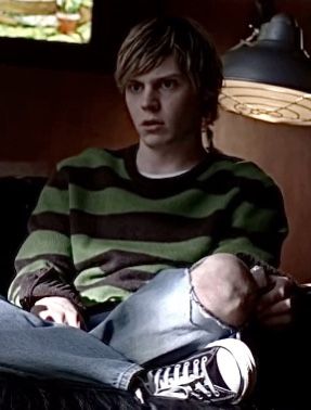 a young man sitting on top of a couch next to a lamp and a window