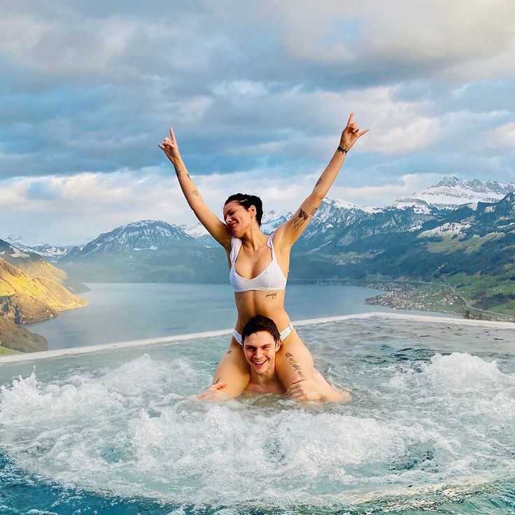 a man and woman are in the water on their stomachs, with mountains in the background