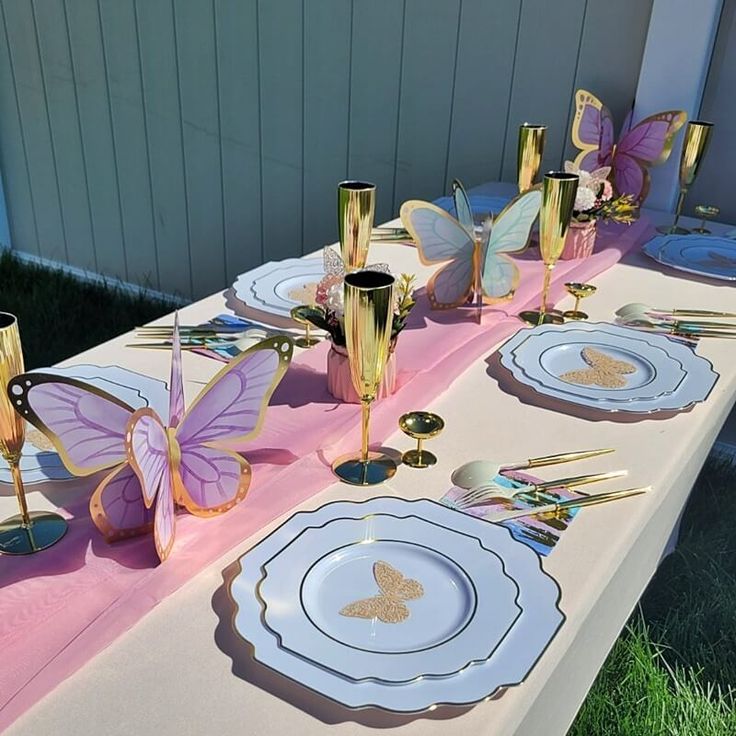 a table set up with gold and pink plates, silverware and butterfly napkins