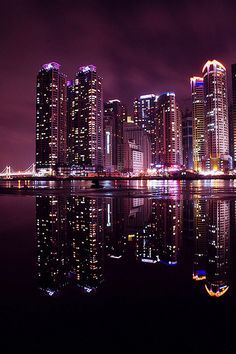 the city is lit up at night and reflecting in the water