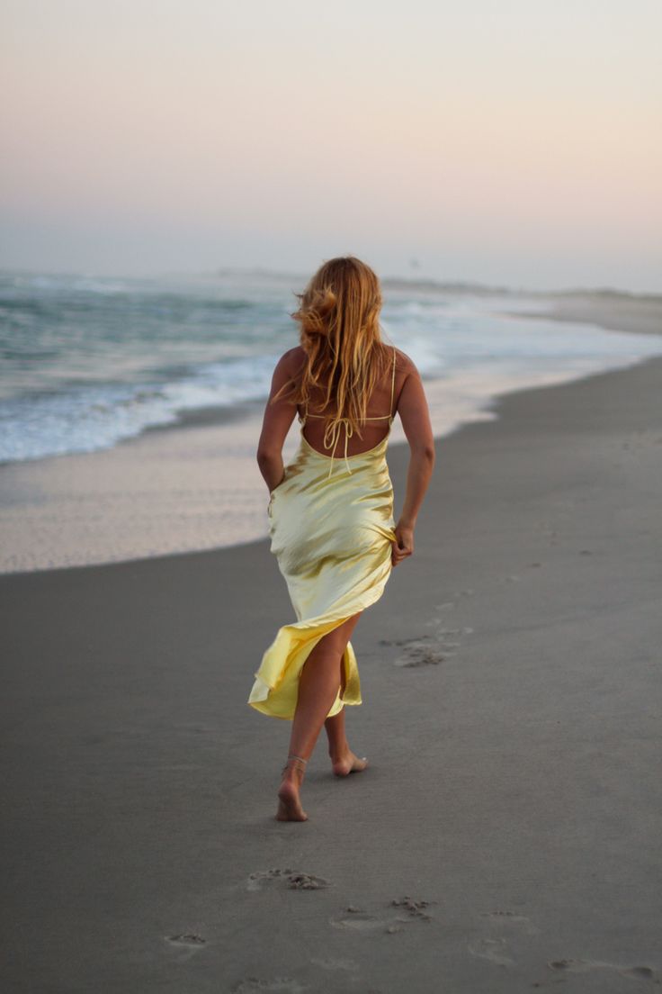 a woman in a yellow dress walking on the beach