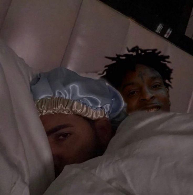 two people laying in bed with white sheets and blankets on their heads, one person has his head wrapped around the other