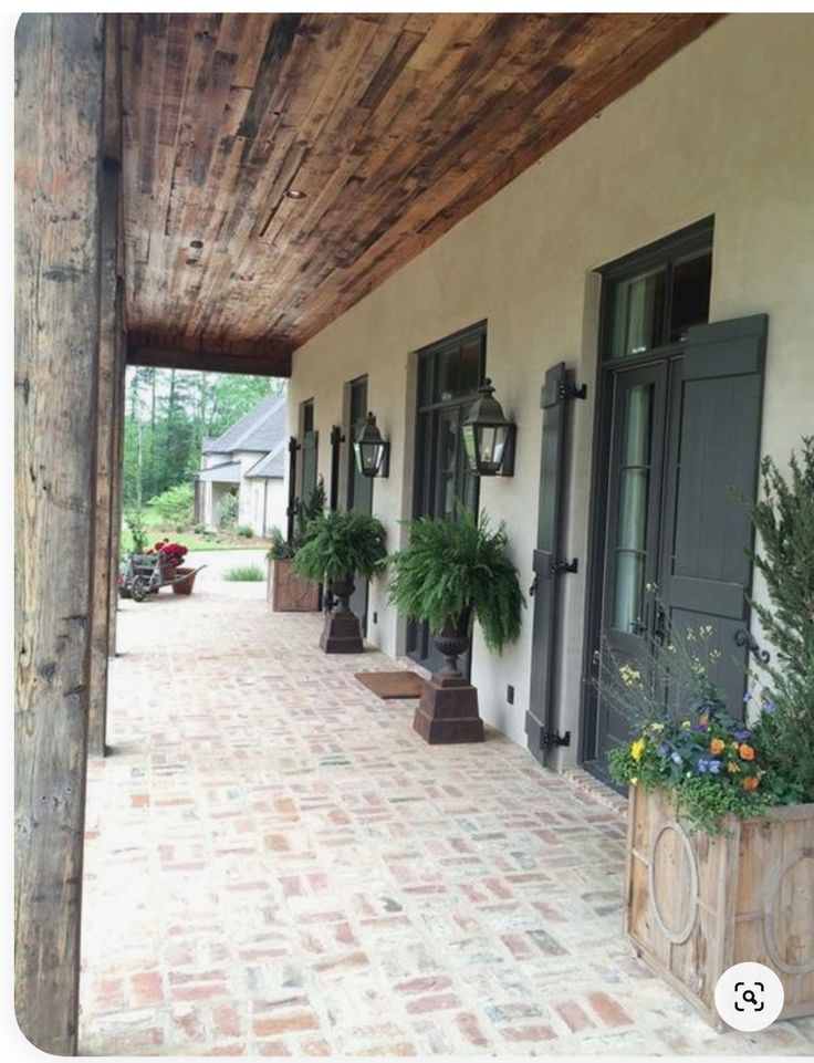 the porch is lined with potted plants and wooden posts, along with brick pavers flooring