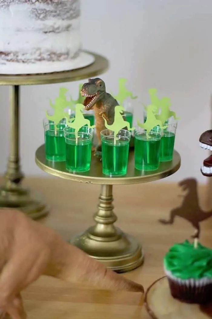 dinosaur cupcakes with green frosting on a cake stand