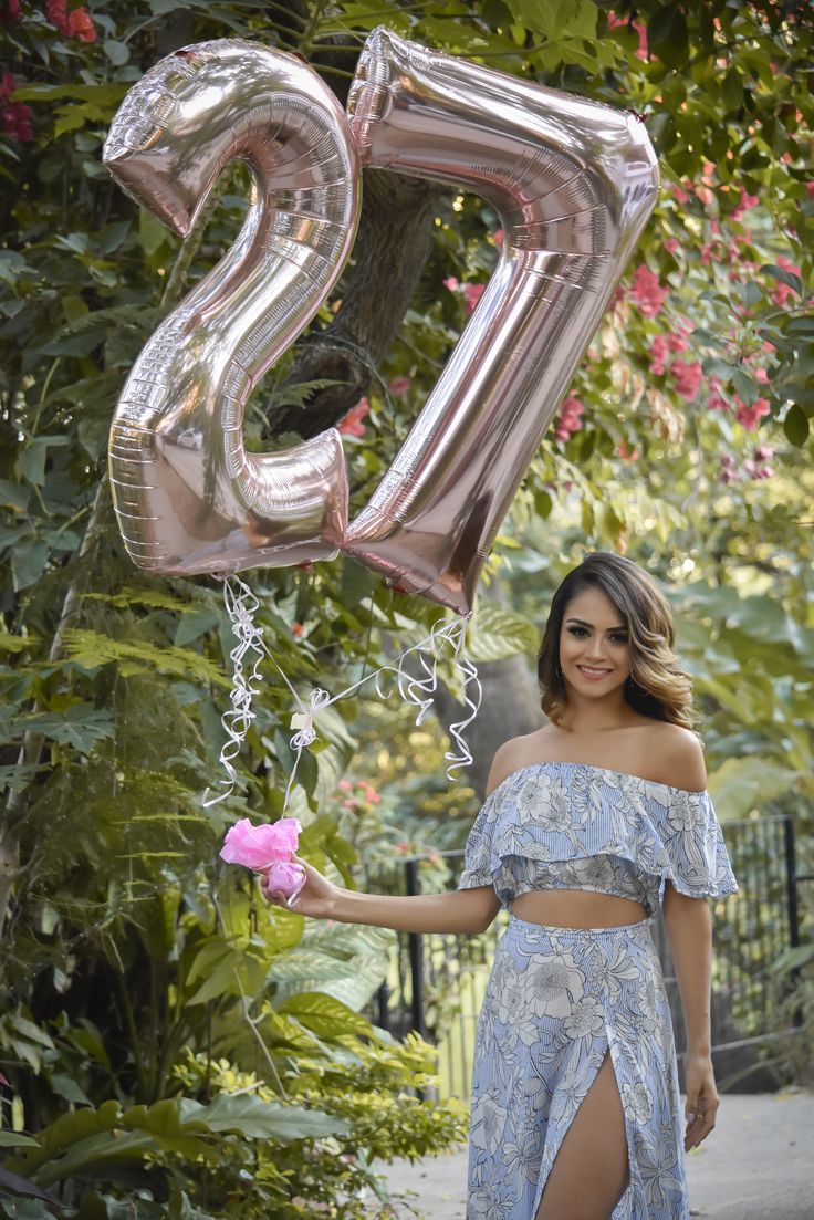 a woman in a blue dress holding a pink flower and number 25 balloon with the number twenty five on it