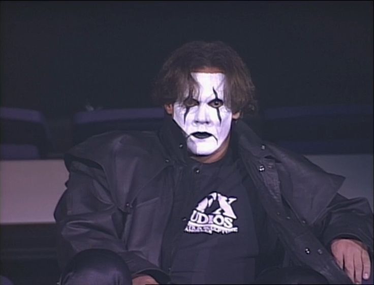 a man with his face painted white sitting in a chair wearing a black shirt and jacket