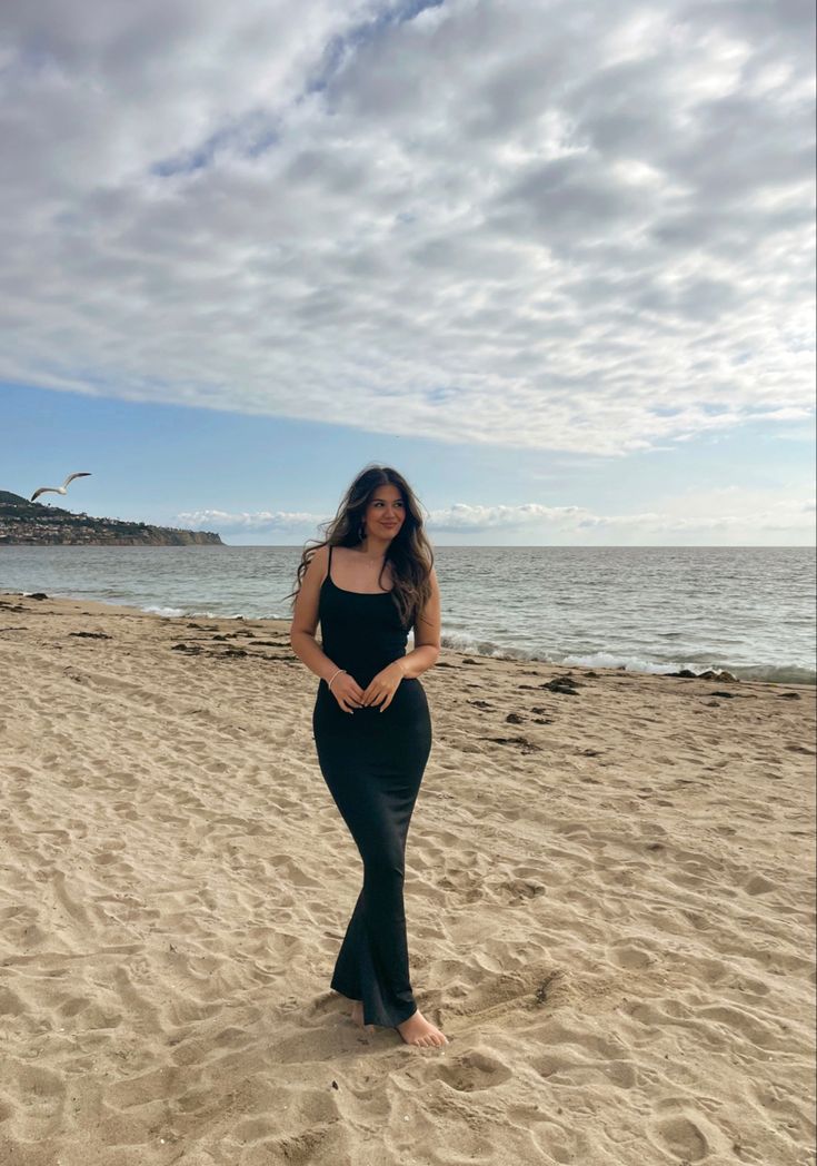 a woman standing on top of a sandy beach next to the ocean with clouds in the sky