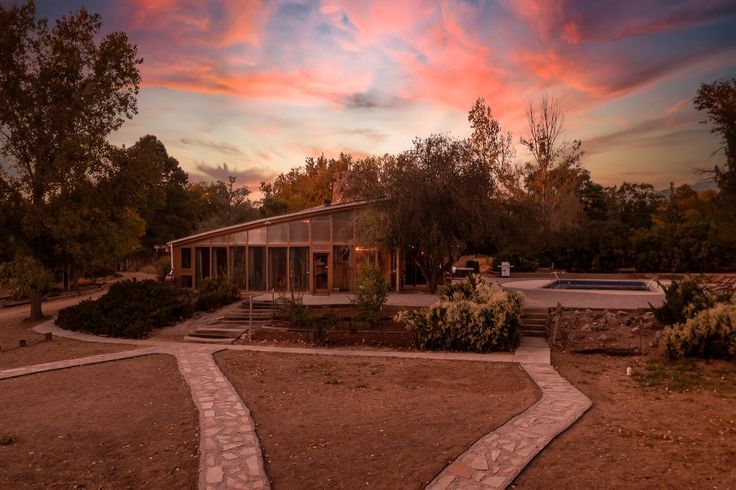 a house with a pool in the middle and trees around it at sunset or dawn