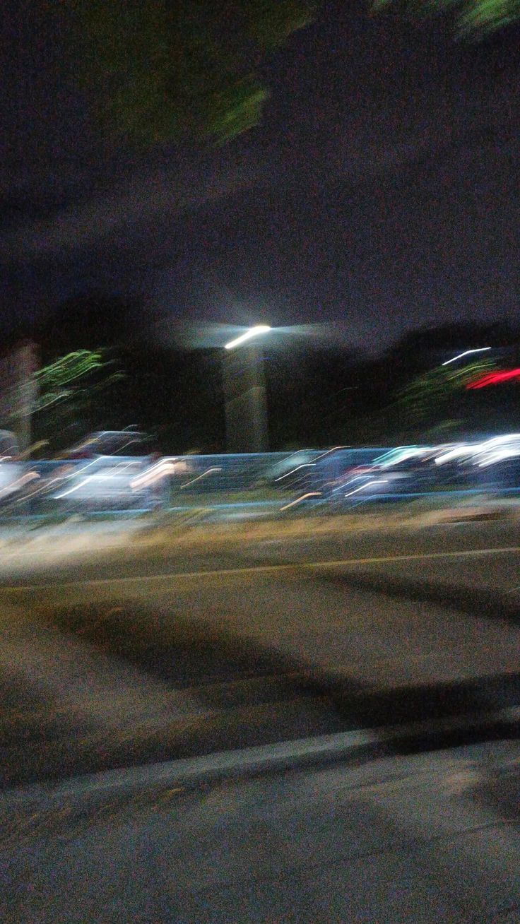 blurry photograph of cars driving down the road at night time with street lights in the background