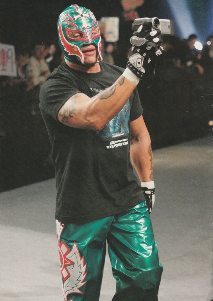 a man in green pants and a black shirt with a wrestling mask on his face