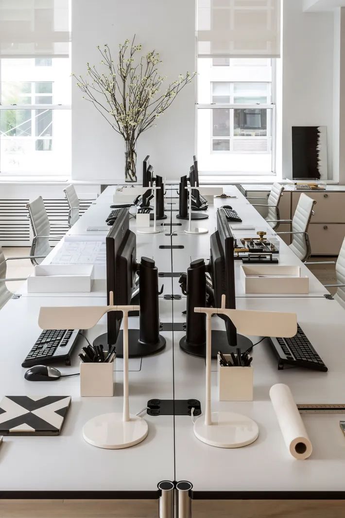 a long table with chairs and computers on it in an office setting that is well lit by large windows