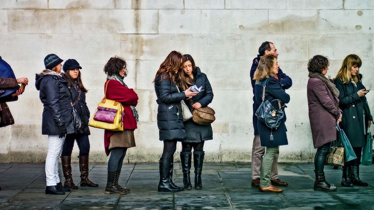 a group of people standing next to each other on the sidewalk looking at their cell phones