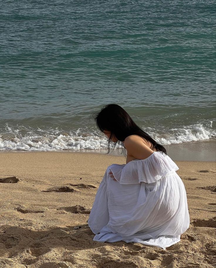 a woman sitting on top of a sandy beach next to the ocean