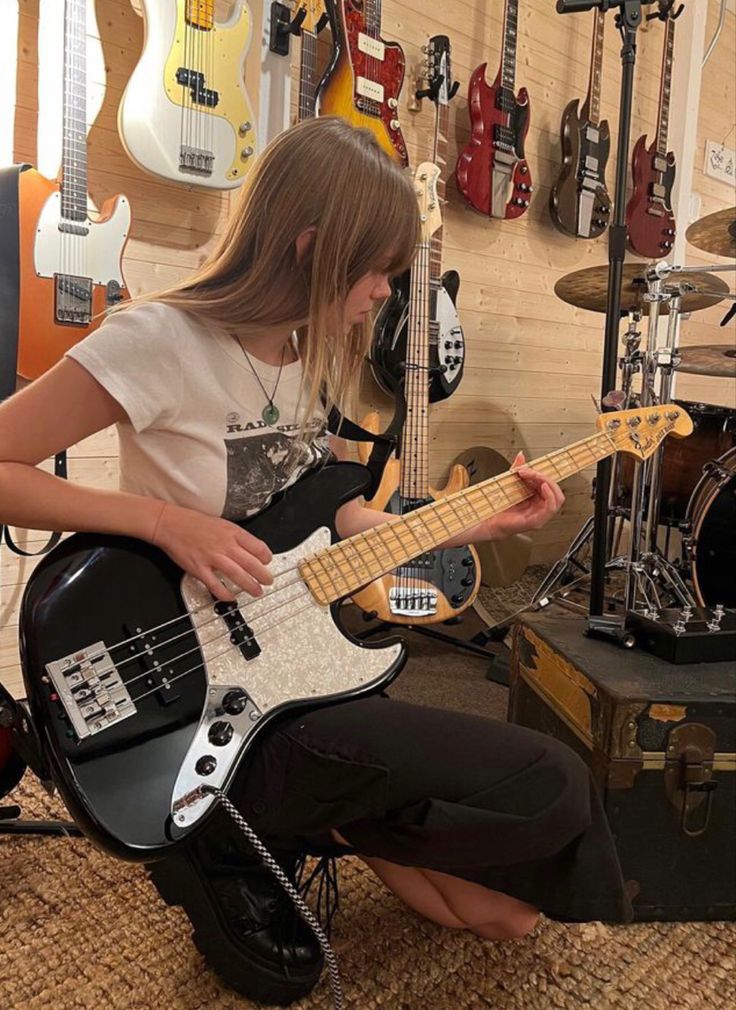 a woman sitting on the floor playing an electric guitar in front of guitars and other musical equipment