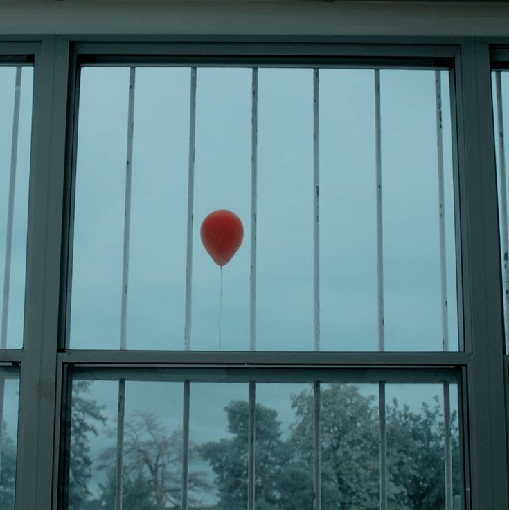 a red balloon floating in the air through a window