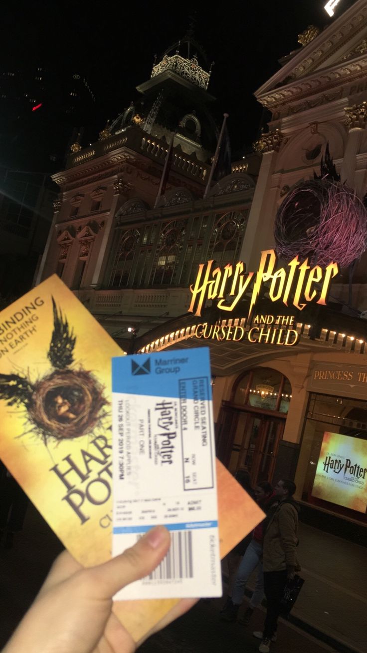 a person holding up a harry potter ticket in front of a building