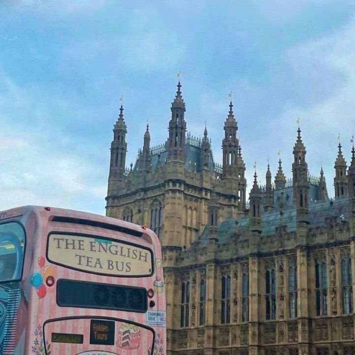 a pink double decker bus parked in front of a large building with tall spires