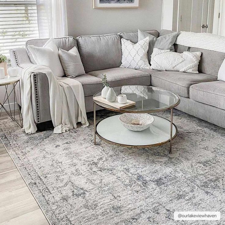 a living room with gray couches, white pillows and a rug on the floor