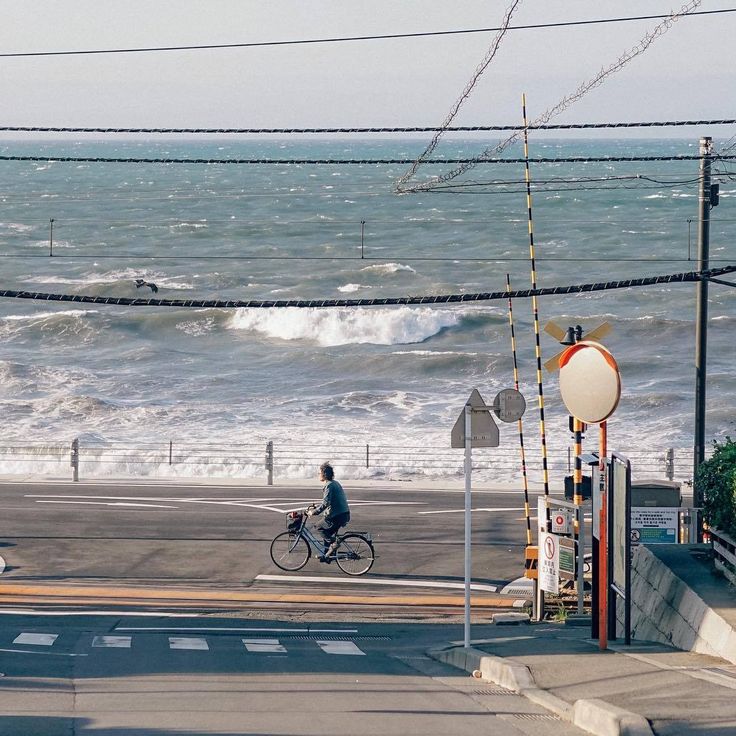 a person riding a bike down the street next to the ocean with waves in the background